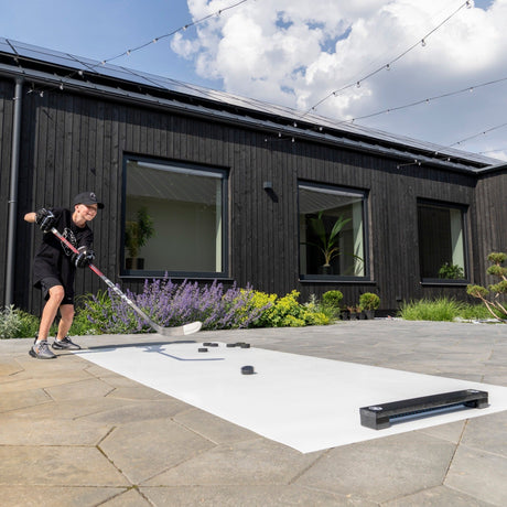 Young hockey player training with a rebounder and roll-up shooting pad on a garden terrace