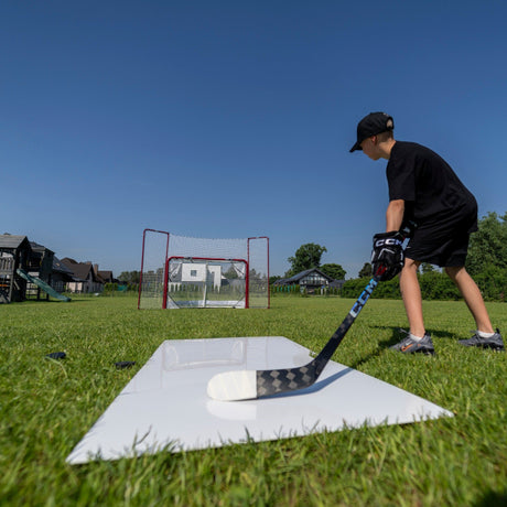 Young hockey player lining up a shot from a shooting pad toward a net in the garden
