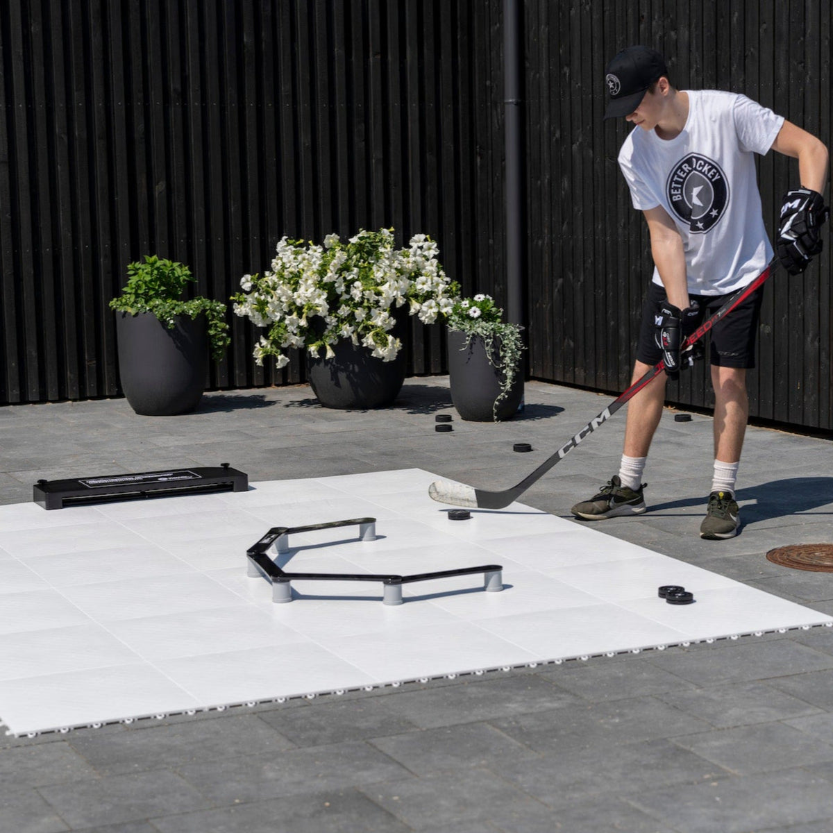 Hockey player practicing stickhandling on flooring tiles with training equipment outdoors