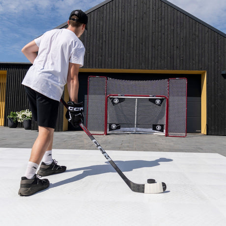 Hockey player practicing shooting accuracy on training tiles toward a net with corner targets