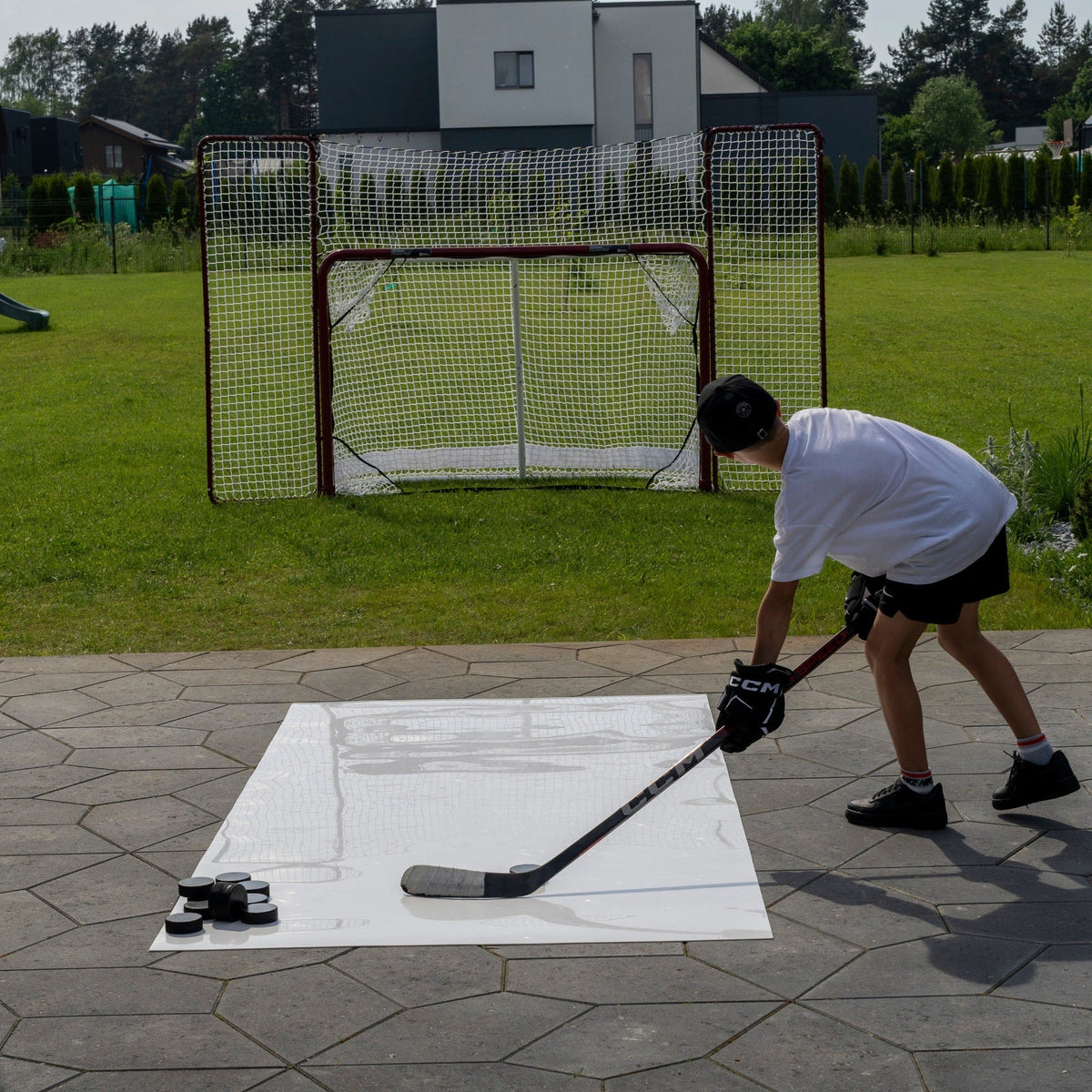 Young hockey player practicing shots on a roll-up shooting pad in a garden with a full-size goal