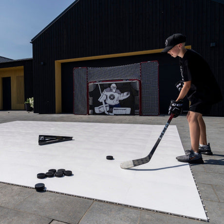 Young hockey player shooting on flooring tiles toward a goal in the garden