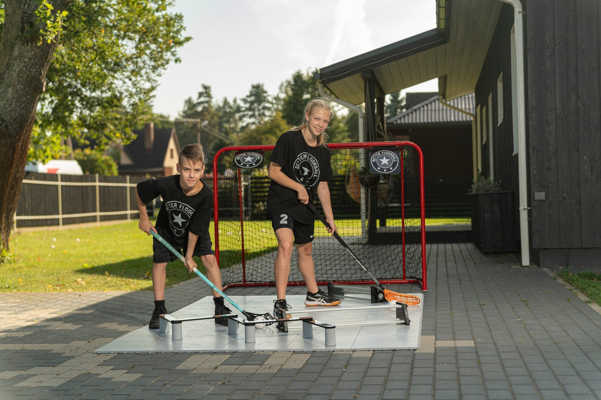 Two kids practising passing and shooting at the floorball goal