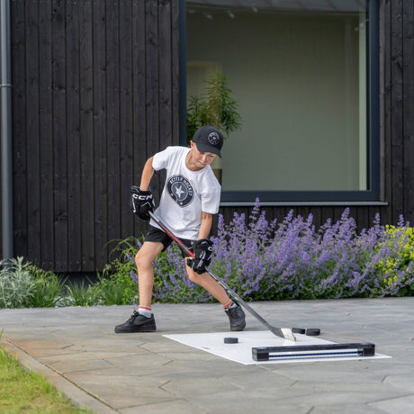 Young hockey player passing pucks with the Extreme Hockey Rebounder on a garden terrace