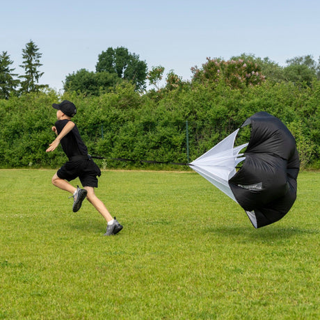 Young hockey player sprinting outdoors with a speed chute during off-ice training