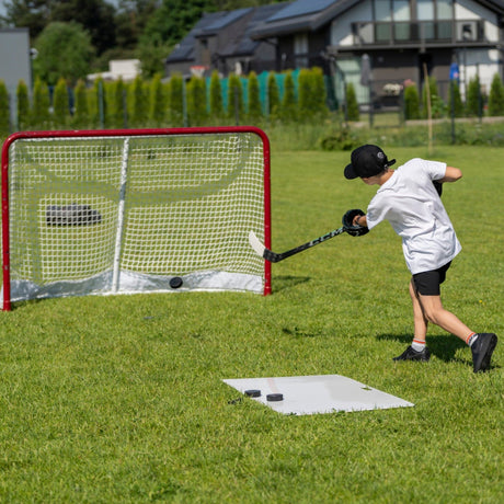 Young hockey player shooting pucks toward a goal in a garden with a shooting pad on the grass