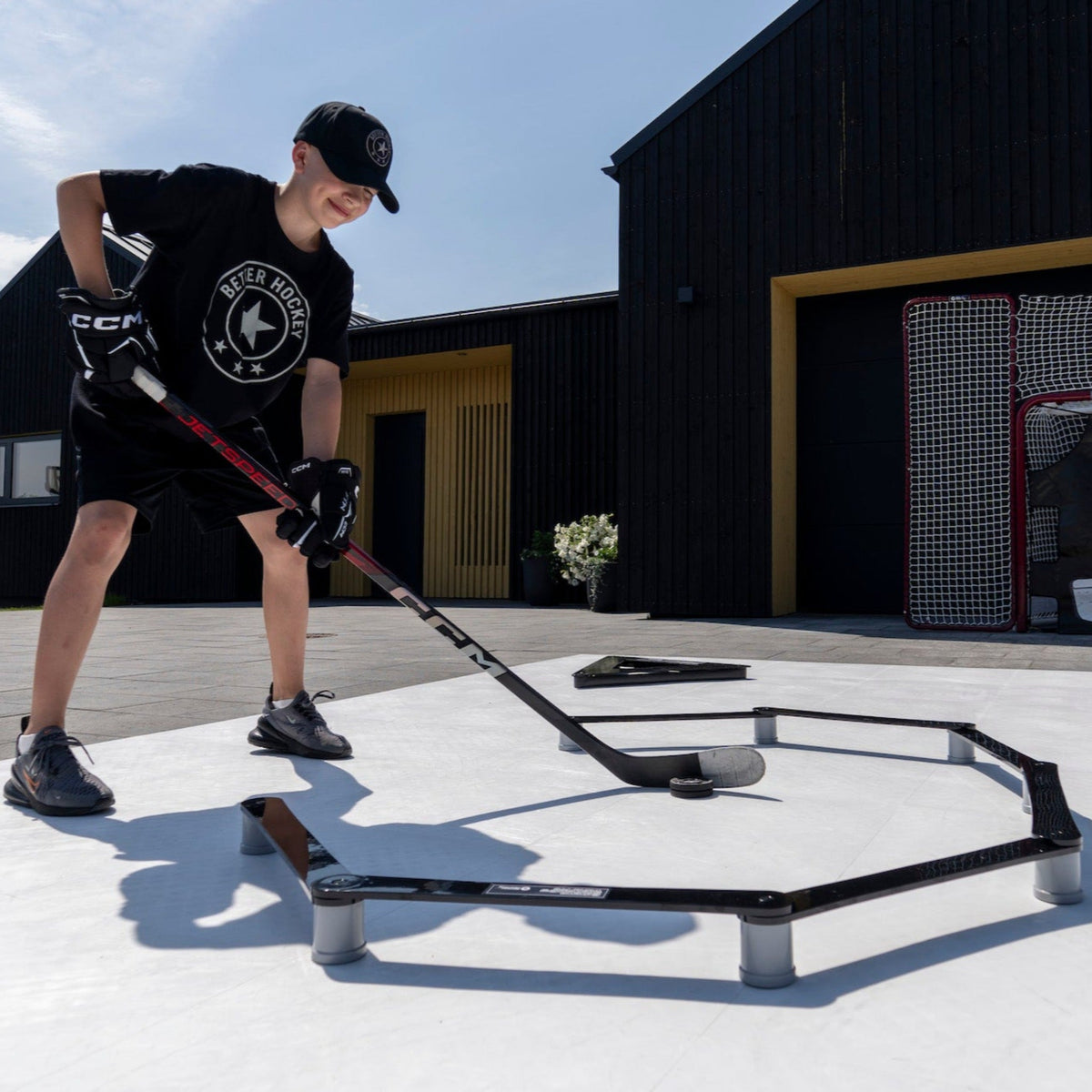 Young hockey player stickhandling with the Extreme Stickhandling Trainer outdoors near a hockey net in a garden setting