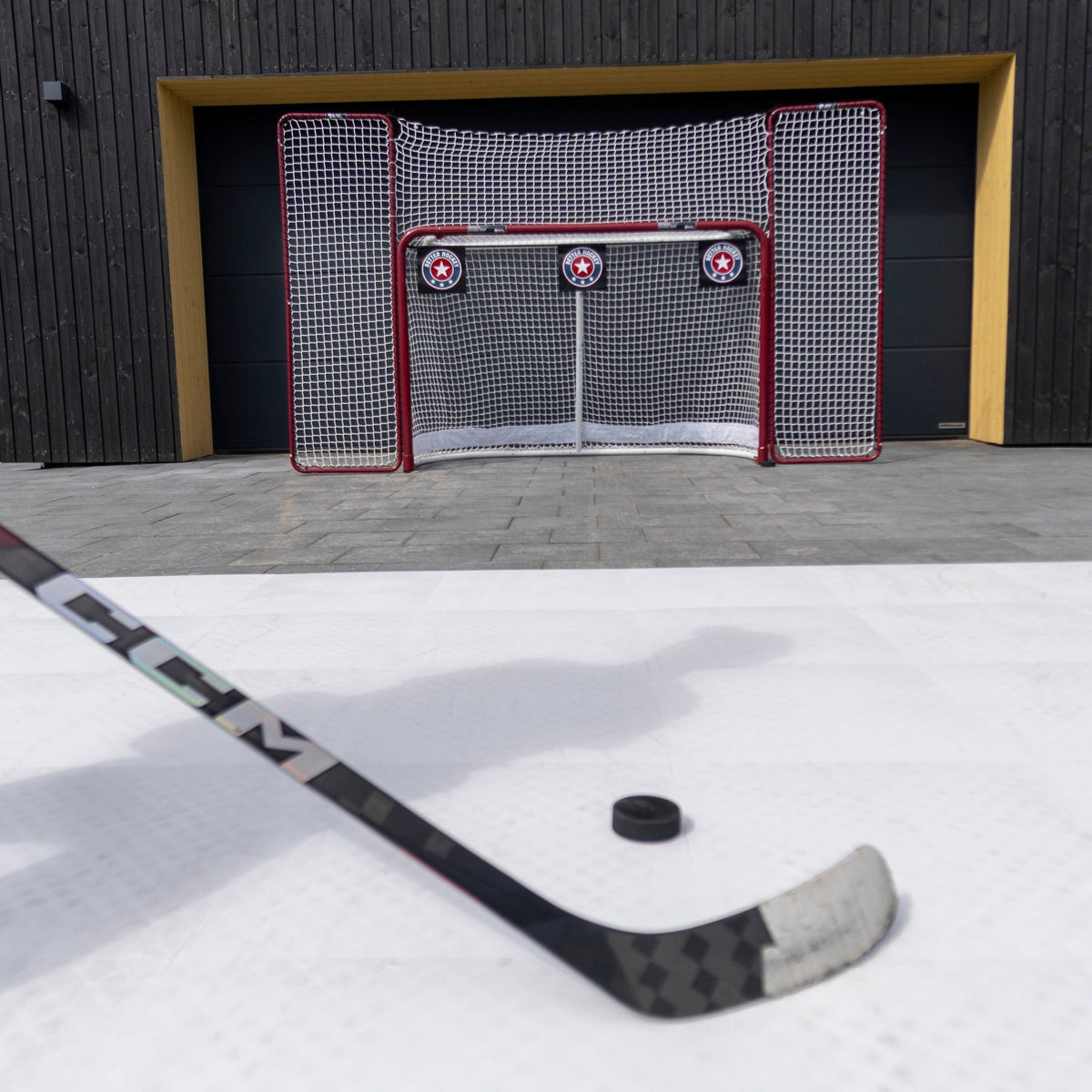 Hockey stick and puck on a shooting pad with shooting targets in a net in the garden